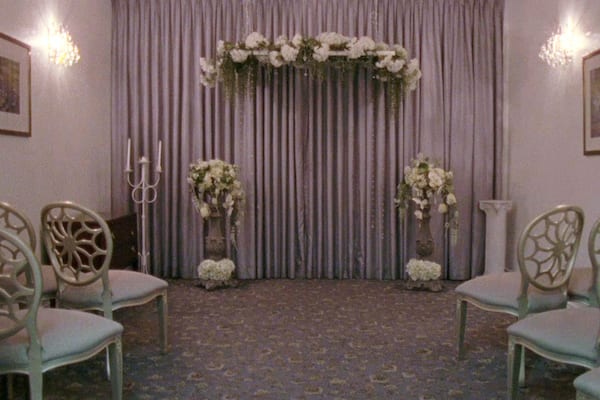 Film still with a mauve ceremonial altar and chairs facing forward.