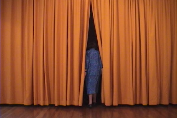 Person in blue outfit exits a stage through a set of vivid orange curtains.