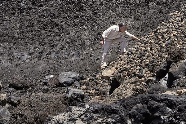 Person wearing all white climbs up a slope of dark, rough rocks.