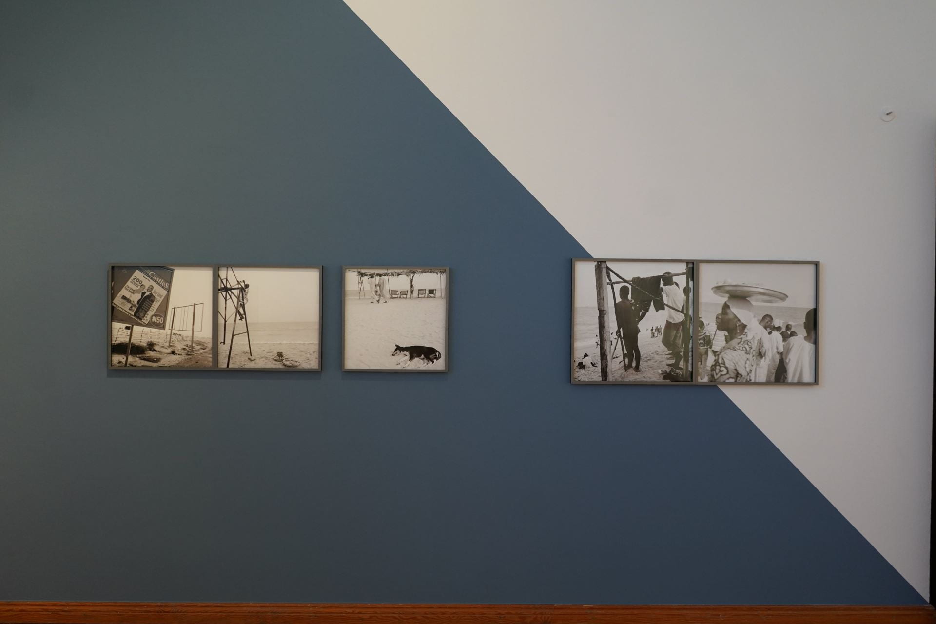 Five black and white photographs hang on a wall painted with blue on a diagonal