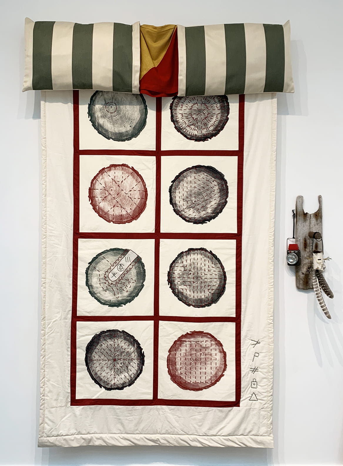 Red, green, and cream colored quilt hangs off wall. Square panels show prints of tree rings