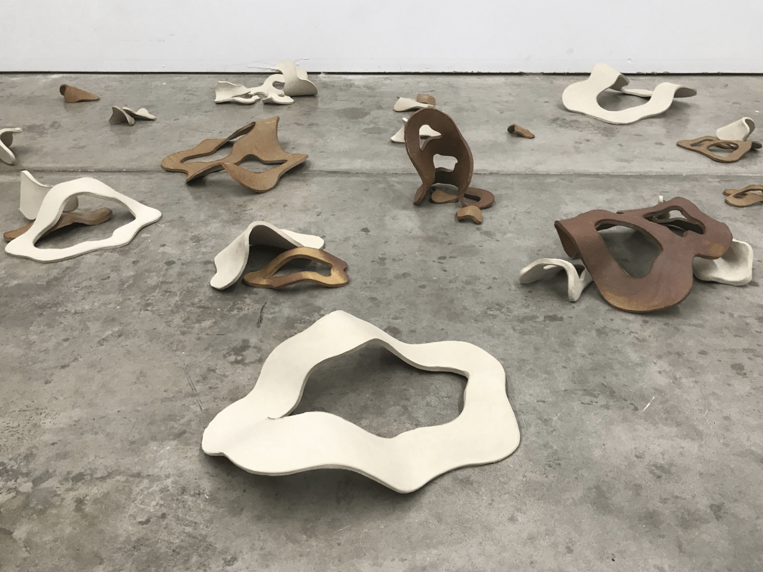 Wavy white, tan, and brown sculptural forms sit on a concrete floor.